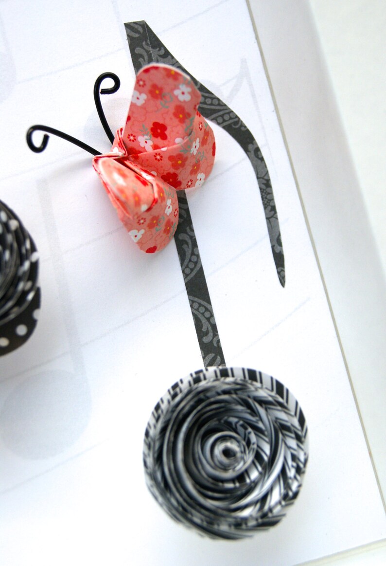 May include: A black and white paper flower with a black and white patterned background. A pink and white butterfly with a floral pattern is attached to a black musical note.