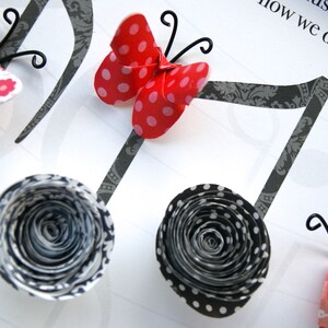 May include: A craft project featuring paper butterflies and flowers with black and white polka dot patterns, attached to black musical notes. The text "music life plays how we dance to it." is written on the white background.