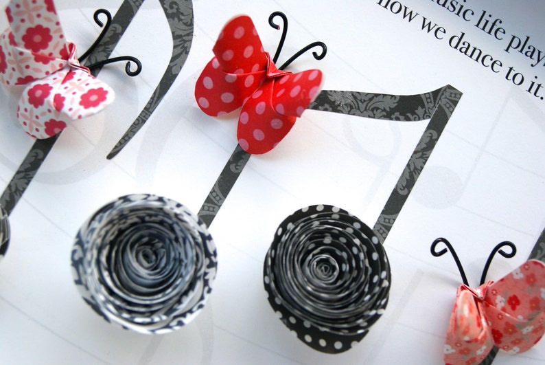 May include: A craft project featuring paper butterflies and flowers with black and white polka dot patterns, attached to black musical notes. The text "music life plays how we dance to it." is written on the white background.