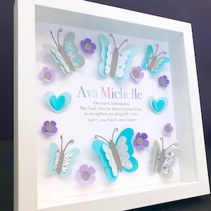 Könnte beinhalten: Ein weißer Rahmen mit einem hellblauen und grauen Schmetterlingsdesign. Der Rahmen enthält den Text "Ava Michelle" und eine Botschaft zur Konfirmation.