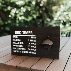 May include: A dark brown wooden sign with a bottle opener attached. The sign has white text that reads "BBQ TIMER" and lists different levels of doneness for meat, with corresponding beer consumption recommendations. The text reads: "RARE: 1 BEER, MEDIUM: 3 BEERS, WELL DONE: 6 PACK, PORK RIBS: 12 PACK, PULLED PORK: 30 PACK, BRISKET: DRUNK AS HELL."