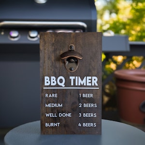 May include: A wooden sign with a bottle opener and a BBQ timer. The sign has a dark brown wood finish and white text that reads "BBQ TIMER". The timer is based on the number of beers you drink while grilling.  The text reads: "Rare - 1 Beer, Medium - 2 Beers, Well Done - 3 Beers, Burnt - 4 Beers."