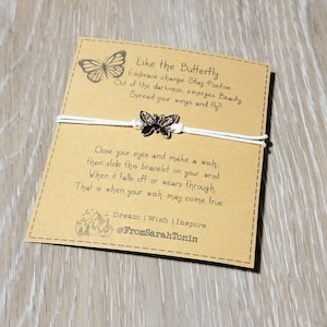 May include: A butterfly charm bracelet on a tan card with the text "Like the Butterfly." The card features a butterfly illustration and inspirational text. The bracelet has a white cord and a silver butterfly charm.
