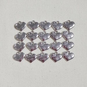 May include: A collection of 15 silver heart-shaped charms with the text "Mother of the Bride" engraved on each charm.