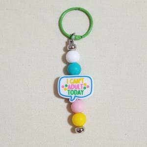 May include: A keychain with a green ring, silver accents, and colorful beads. The keychain features a speech bubble with the text "I CAN'T ADULT TODAY" in blue, yellow, and pink.