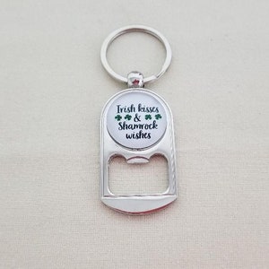 May include: Silver bottle opener keychain with a round, white, and green shamrock design. The design says "Irish kisses & shamrock wishes".