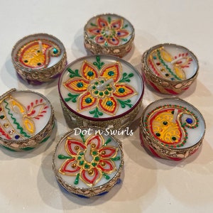 May include: Seven decorative candles with intricate floral and paisley designs. The candles are in ornate, gold-colored holders with colorful accents of red, yellow, green, and blue. The candles are arranged in a circular pattern.