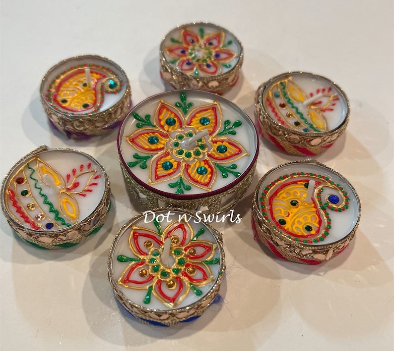 May include: Seven decorative candles with intricate floral and paisley designs. The candles are in ornate, gold-colored holders with colorful accents of red, yellow, green, and blue. The candles are arranged in a circular pattern.
