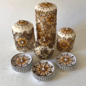 Puede incluir: Conjunto de seis velas con intrincados dise&ntilde;os de henna en dorado y marr&oacute;n. Las velas son de varios tama&ntilde;os, incluyendo velas pilares y velas de t&eacute;. Las velas de t&eacute; tienen una base plateada.