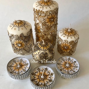 Puede incluir: Conjunto de seis velas blancas en forma de pilar con dise&ntilde;os de henna dorados y negros. Las velas est&aacute;n decoradas con diamantes de imitaci&oacute;n y vienen en tres tama&ntilde;os. El conjunto incluye dos peque&ntilde;as velas de t&eacute;.