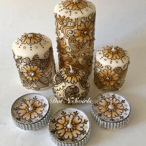 Puede incluir: Conjunto de seis velas blancas en forma de pilar con dise&ntilde;os de henna dorados y negros. Las velas est&aacute;n decoradas con diamantes de imitaci&oacute;n y vienen en tres tama&ntilde;os. El conjunto incluye dos peque&ntilde;as velas de t&eacute;.