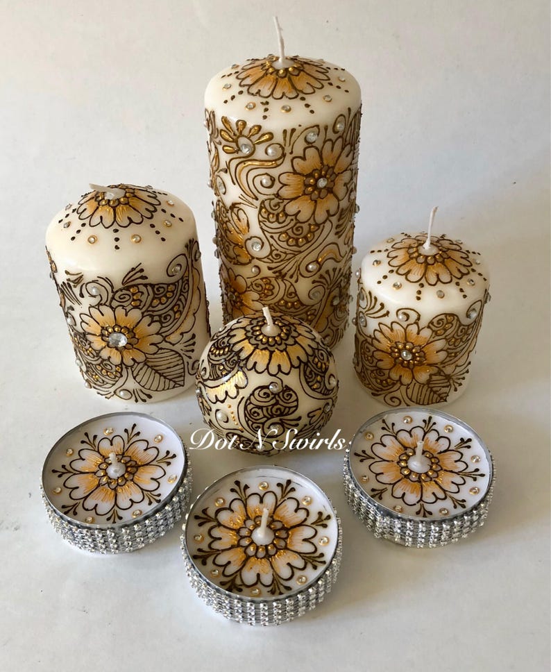 Puede incluir: Conjunto de seis velas blancas en forma de pilar con dise&ntilde;os de henna dorados y negros. Las velas est&aacute;n decoradas con diamantes de imitaci&oacute;n y vienen en tres tama&ntilde;os. El conjunto incluye dos peque&ntilde;as velas de t&eacute;.