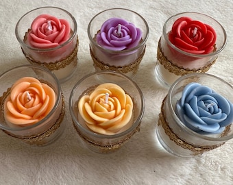 Puede incluir: Seis velas con forma de rosa en candelabros de cristal transparente. Las velas son en tonos rosa, morado, rojo, naranja, amarillo y azul. Cada candelabro está decorado con una banda de lentejuelas doradas en la base.