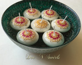 May include: Eight white floating candles with pink and gold floral designs and rhinestones in a teal bowl with a swirling pattern.  "Dot N Swirls" is written in cursive at the bottom of the image.