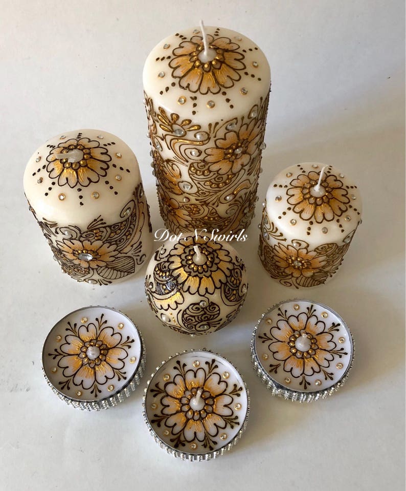 Puede incluir: Conjunto de seis velas blancas en forma de pilar con dise&ntilde;os de henna dorados y marrones y diamantes de imitaci&oacute;n. El conjunto incluye tres velas de pilar y tres velas de t&eacute;.