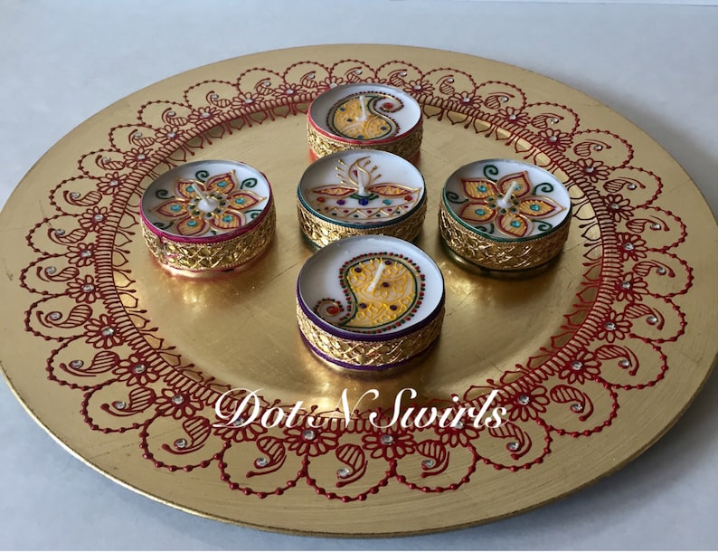 May include: A gold-colored decorative plate with a red henna-style border and five small, round candles. The candles have intricate designs and gold-colored rims. The text "Dot N Swirls" is visible on the plate.