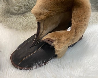 May include: Brown leather slipper with a zipper and a fluffy brown fur lining. The slipper is on a white fluffy surface.