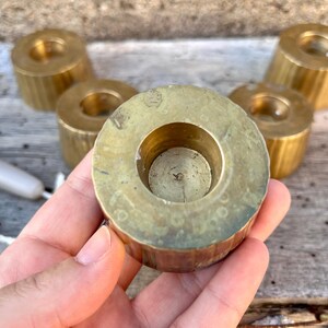 May include: A set of five cylindrical brass candle holders with a vertical ribbed texture on the sides. Each holder features a circular opening in the center for a taper candle. The brass has a polished finish with some natural patina and wear.