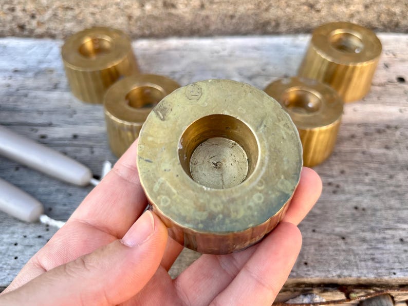 May include: A set of five cylindrical brass candle holders with a vertical ribbed texture on the sides. Each holder features a circular opening in the center for a taper candle. The brass has a polished finish with some natural patina and wear.
