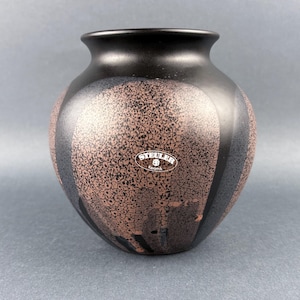 May include: A black ceramic vase with a speckled brown and black design. The vase has a rounded shape with a narrow neck and a small white sticker with the text "STEULER Keramik".