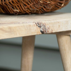 May include: A light wood bench with a natural wood grain finish. The bench has a rustic, distressed look with a small crack in the top surface. The bench is made of solid wood and has a simple, elegant design.