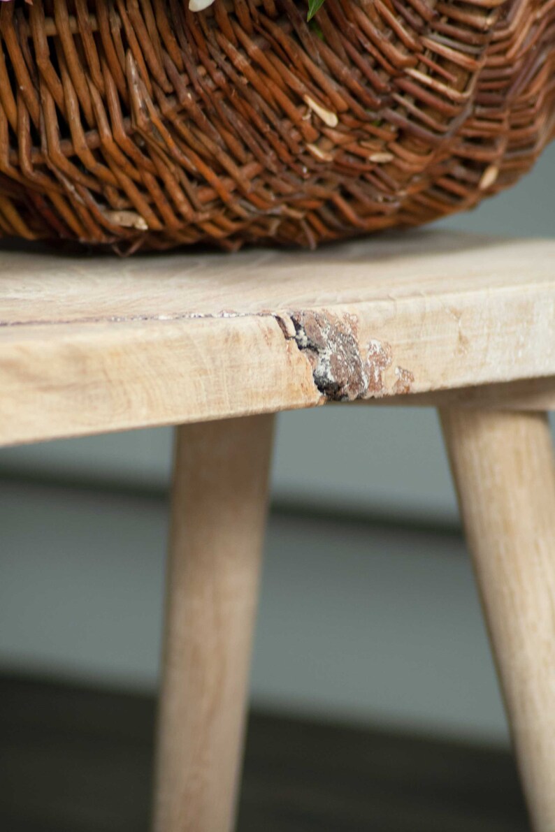 May include: A light wood bench with a natural wood grain finish. The bench has a rustic, distressed look with a small crack in the top surface. The bench is made of solid wood and has a simple, elegant design.