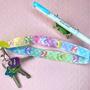 May include: A colorful lanyard with a rainbow pattern and cartoon sharks. The lanyard has a key ring with three keys attached. A blue highlighter with the text "Mildliner Double Ended" is also in the image.