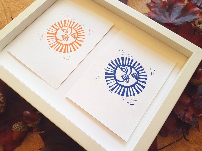May include: Two framed prints of sun faces, one in orange and one in blue, with a white background.