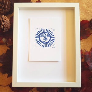 May include: A framed print of a blue sun and moon design. The sun and moon are stylized with faces and are surrounded by rays.