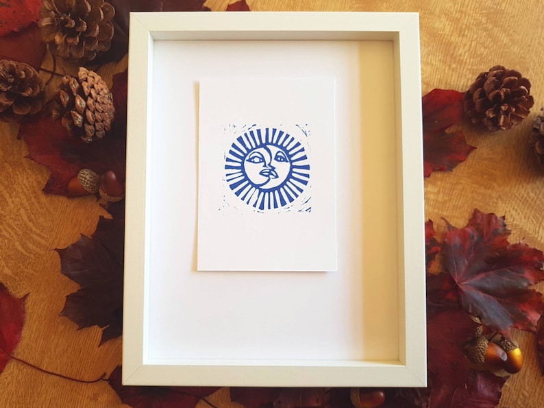 May include: A framed print of a blue sun and moon design. The sun and moon are stylized with faces and are surrounded by rays.