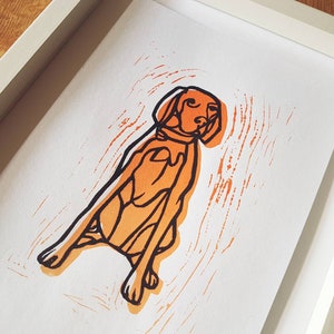 May include: A framed print featuring a stylized orange and black illustration of a dog. The dog is depicted in a seated position with a collar. The artwork is set against a white background within a white frame.