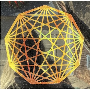 May include: A geometric, golden-colored design with a complex, interconnected pattern. The shape is an octagon with a central circular opening. The design has a metallic sheen, reflecting light and creating a shimmering effect. The background is dark and textured.