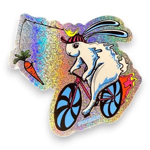 Pegatina troquelada resistente a la intemperie, brillante y con polvo de hadas de un conejito en bicicleta persiguiendo una zanahoria