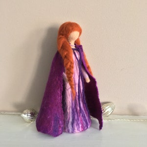 May include: A felt doll with long, braided red hair wearing a purple dress and a matching cape.