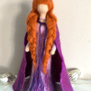 May include: A felt doll with long braided red hair, wearing a purple dress and a matching cape.
