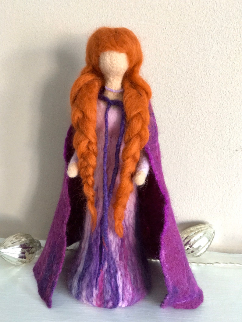 May include: A felt doll with long braided red hair, wearing a purple dress and a matching cape.
