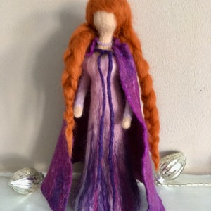 May include: A felt doll with long, braided red hair wearing a purple and pink dress and a purple cape.