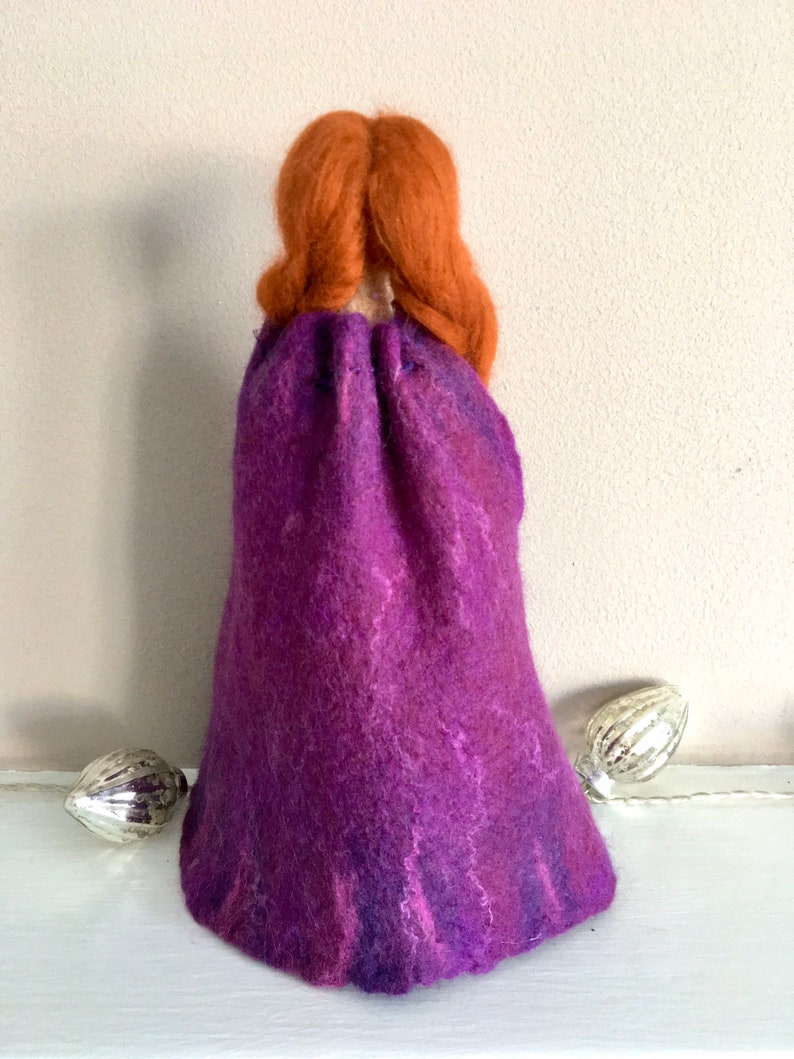 May include: A felt doll with long, braided, auburn hair wearing a purple, hand-felted cloak.