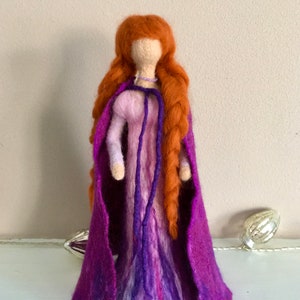 May include: A felt doll with long, braided red hair wearing a purple dress and a matching cape.