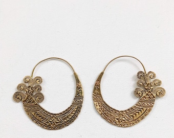 May include: A pair of gold hoop earrings with intricate, detailed designs. The earrings are made of metal and have a circular shape with a decorative floral pattern.