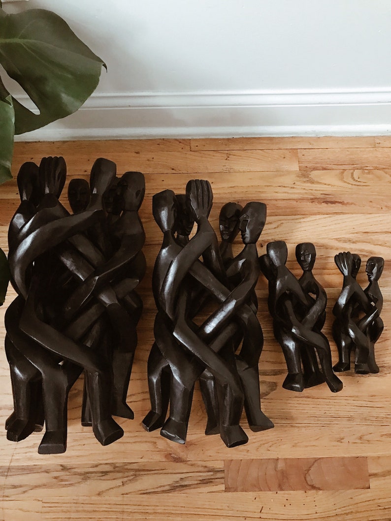 May include: A set of four wooden sculptures of intertwined figures. The sculptures are made of dark wood and are arranged in a row, with the largest sculpture in the center and the smallest sculptures on either end.