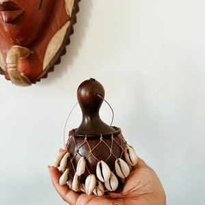 以下が含まれることがあります： 茶色のひょうたんの形をした小さな打楽器。茶色の紐の網と白い貝殻がぶら下がっている。