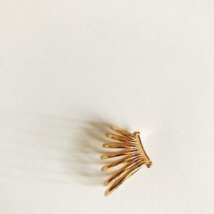May include: Gold ear cuff with a fan-shaped design. The cuff is made of multiple thin metal pieces that are connected together.