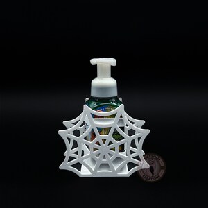 May include: White plastic spiderweb soap dispenser holder. The holder is shaped like a spiderweb and has a small opening in the center for the soap dispenser to fit through. The soap dispenser is not included.