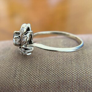 Puede incluir: Un anillo de plata con un dise&ntilde;o floral y piedras transparentes. El anillo est&aacute; sobre un fondo de tela marr&oacute;n.