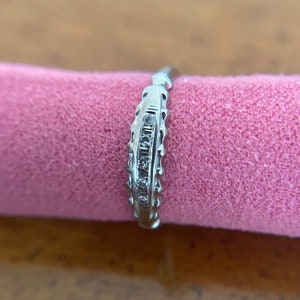 Op de afbeelding: Een zilveren bandring met een rij kleine diamanten die in het midden zijn gezet.
