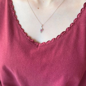 Op de afbeelding: Een zilveren ketting met een klein roze edelsteen hanger in de vorm van een hart.