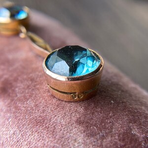 Op de afbeelding: Een gouden ketting met twee blauwe topaas edelstenen. De ketting heeft een delicate ketting en de edelstenen zijn gezet in goud.