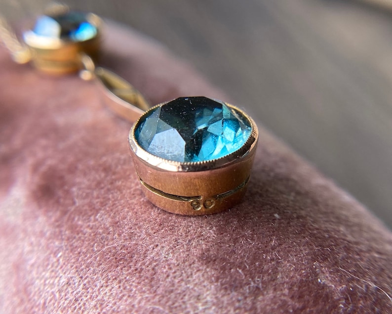 Op de afbeelding: Een gouden ketting met twee blauwe topaas edelstenen. De ketting heeft een delicate ketting en de edelstenen zijn gezet in goud.