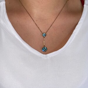 Op de afbeelding: Een gouden ketting met een delicaat hangertje met twee ronde blauwe edelstenen.